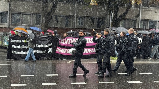 Polizisten laufen vor den Demonstrierenden im Regen