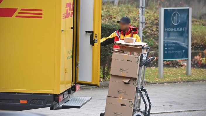 DHL Paketzusteller mit Paketen vor einem geöffneten DHL-Auto