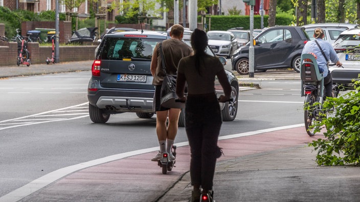  Ein Mann und eine Frau fahren auf E-Scootern auf einem Fahrradweg