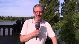 Eine Person mit Mikro in der Hand steht draußen in der Sonne