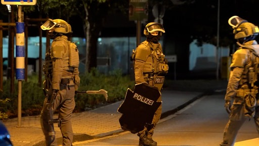 Mehrere Einsatzkräfte stehen mit einem Schild an einer Straße