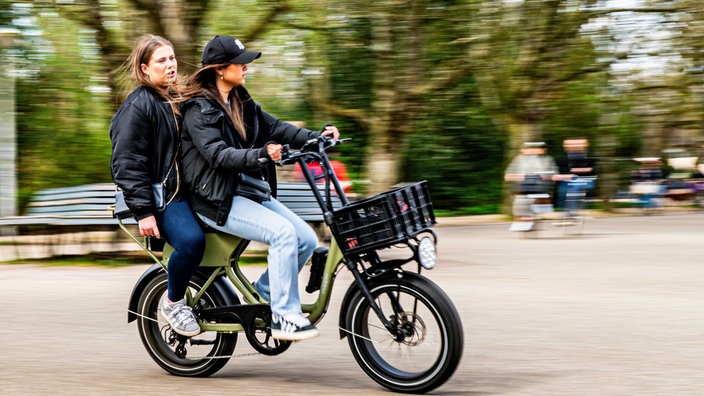 Zwei Frauen fahren mit einem Fatbike durch den Park