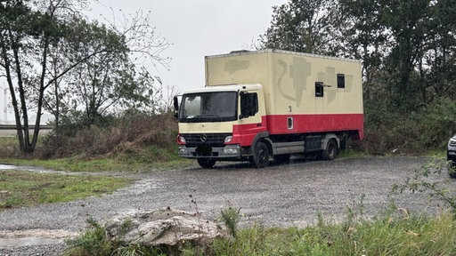Ein beig-roter Lkw auf einem Schotterparkplatz