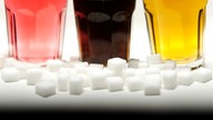 Zuckerwürfel und drei Gläser mit bunten Softdrinks