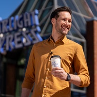Moderator Sven Kroll hält einen Kaffebecher in der Hand und lächelt.