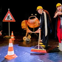 Zwei Opernsänger*innen in Arbeitskleidung mit Baustellen-Bühnenbild.