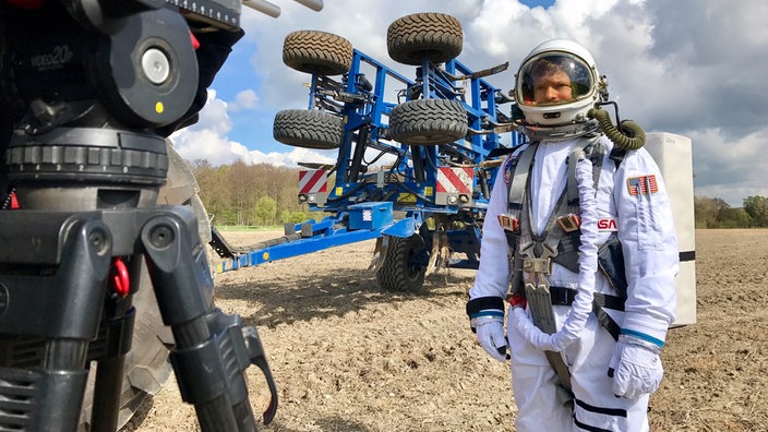 Astronaut auf einem Acker, davor eine Fernsehkamera