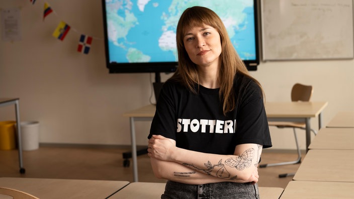 Porträtbild von Jenni im Klassenraum, auf ihrem T-Shirt steht "Stottern" mit Herzen in den Buchstaben