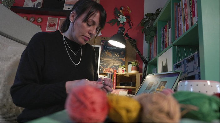 Designerin Inga Borges hält Häkel Nadeln in der Hand, vor ihr sind Woll-Knäule zu sehen. 