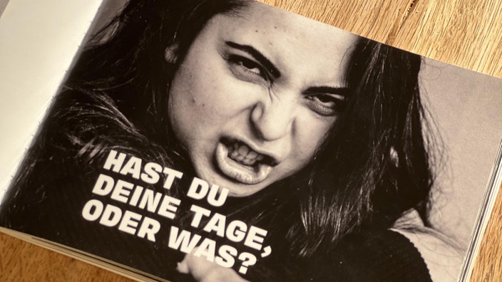 Ein Foto in einem Buch mit einer wütenden Frau mit der Unterschrift „Hast du deine Tage?“