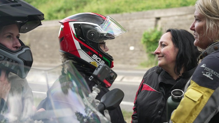 Eine Gruppe von Motorradfahrerinnen mit und ohne Helm steht zusammen.
