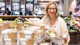 Yvonne Willicks in einem Supermarkt neben einer Kühltruhe mit verschiedenen Fertigsalaten. 
