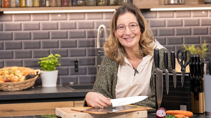 Yvonne Willicks sthet in einer modernen Küche und hält ein scharfes Messer in der Hand. 