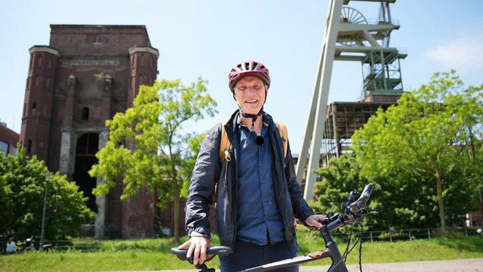Martin Brambach steht mit seinem Fahrrad vor der Zeche Ewald und lacht in die Kamera