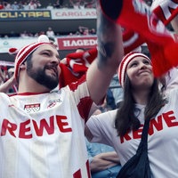 Ein Mann und eine junge Frau in Trikots des FC Köln stehen im Stadion und jubeln