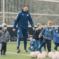 Ein Trainer in Schalke-Trainingsanzug mit vielen Kinder auf dem Fußballplatz