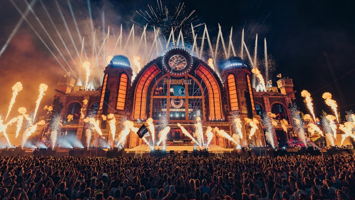 Ein großes Publikum steht vor der Parookaville-Bühne und feiert. Laser-und Feuerstrahler erhellen die Bühne.