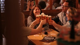 Besucher einer Kneipe sitzen am Tischen und stoßen mit Kölsch an