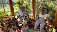 Zwei große Stoffosterhasen sitzen auf einem Stapel Holzscheite in einer osterlich dekorierten Holzhütte.