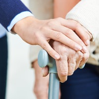 Frau hält die Hand mit einer Seniorin und ihrem Gehstock.