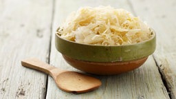 Sauerkraut in einer Schüssel, daneben eine Holzlöffel.