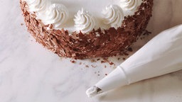 Buttercremetorte mit Schokoraspeln, daneben Spritzbeutel