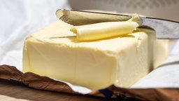 Butter wird mit einem Messer abgehobelt.