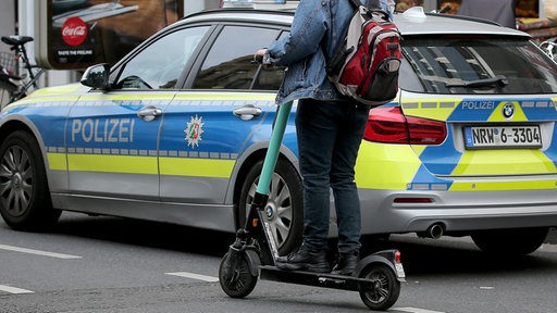 Ein E-Scooter-Fahrer fährt an einem Polizeiauto vorbei.