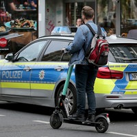 Ein E-Scooter-Fahrer fährt an einem Polizeiauto vorbei.