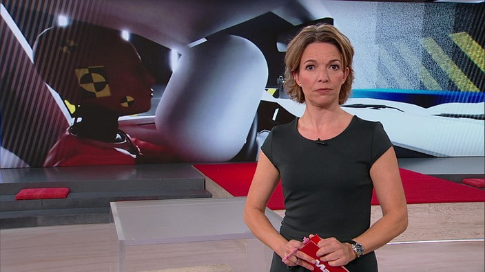  Anna Planken steht im Markt-Studio. Im Hintergrund wird eine Abbildung vom Innenraum eines Autos dargestellt.