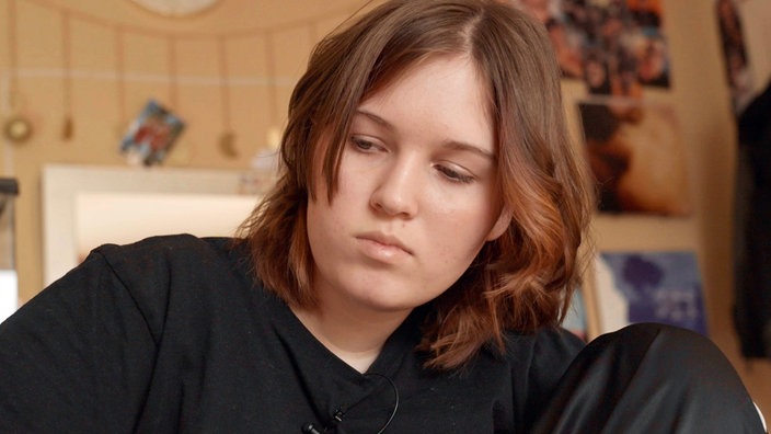 Ein Mädchen mir braunen schulterlangen Haaren guckt betrübt.