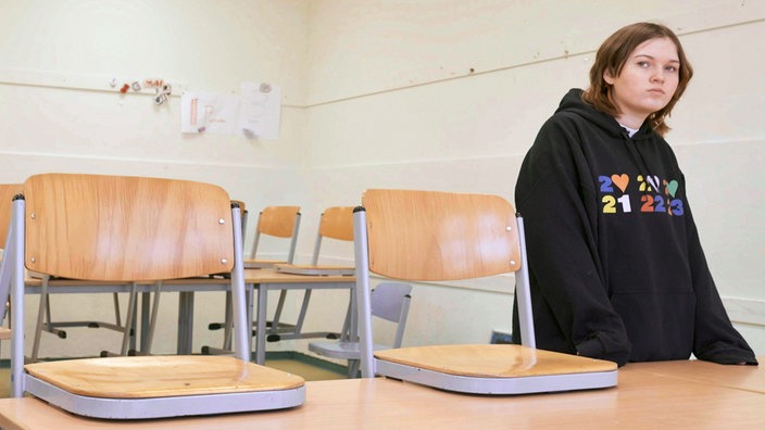 Ein Mädchen steht in einem leerem Klassenraum mit betrübten Blick.