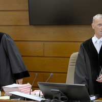 Zwei Männer in Richterkutte stehen vor dem Richterpult in einem Gerichtssaal.