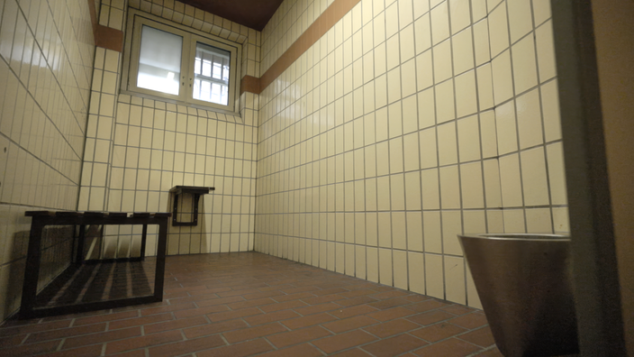 Eine Gefängniszelle mit einem Bett, einem Waschbecken und einer Toilette.