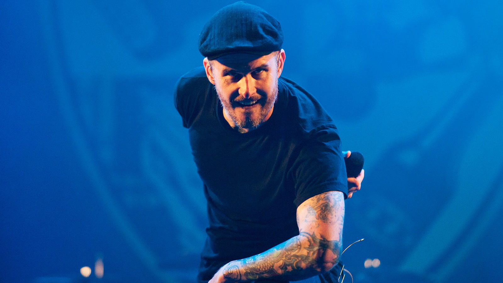 Der Sänger der Band Dropkick Murphys beugt sich nach vorne und hat sein linke Hand mit dem Mikrofon auf dem Rücken verschränkt 