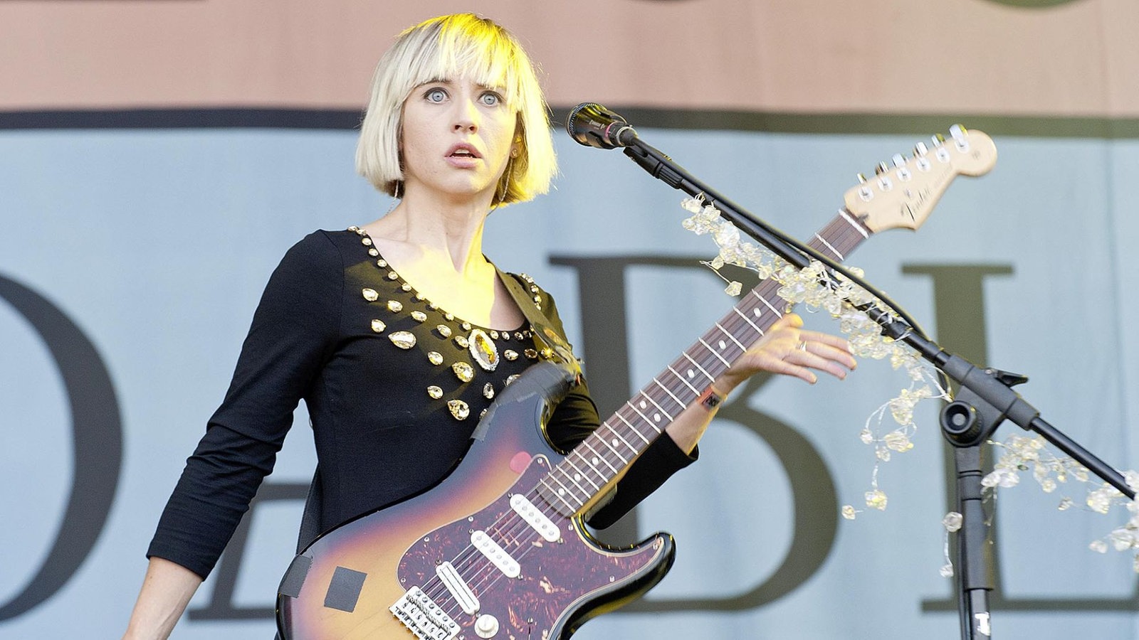 Ritzy Bryan starrt in das Publikum, ansonsten hält sie ihre Gitarre und ein Mikro steht in ihrer Nähe