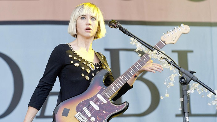 Ritzy Bryan starrt in das Publikum, ansonsten hält sie ihre Gitarre und ein Mikro steht in ihrer Nähe