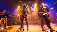 Keyboarder, Sänger und Bassist vorne an der Bühne singen und spielen alle, im Hintergrund auf dem Podest ist der Schlagzeuger zu sehen