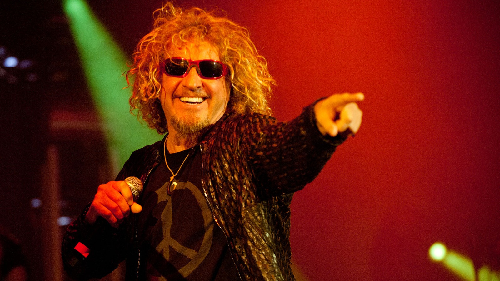 Der Sänger von Chickenfoot hat halb lange wallende Haareund trägt eine rote Sonnenbrille. In der rechten Hand hält er das Mikrofon mit dem linken Finger zeigt er ins Publikum