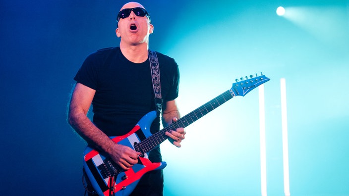 Der Gitarrist der Band hat seine Gitarre umhängen und ist leicht nach vorne gebeugt 