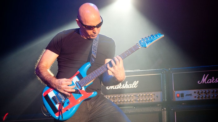 Joe Satriani beugt sich beim Spielen über seine Gitarre