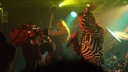 Sänger mit langen Haaren und Zebra-Jacke singt in eine Kamera.