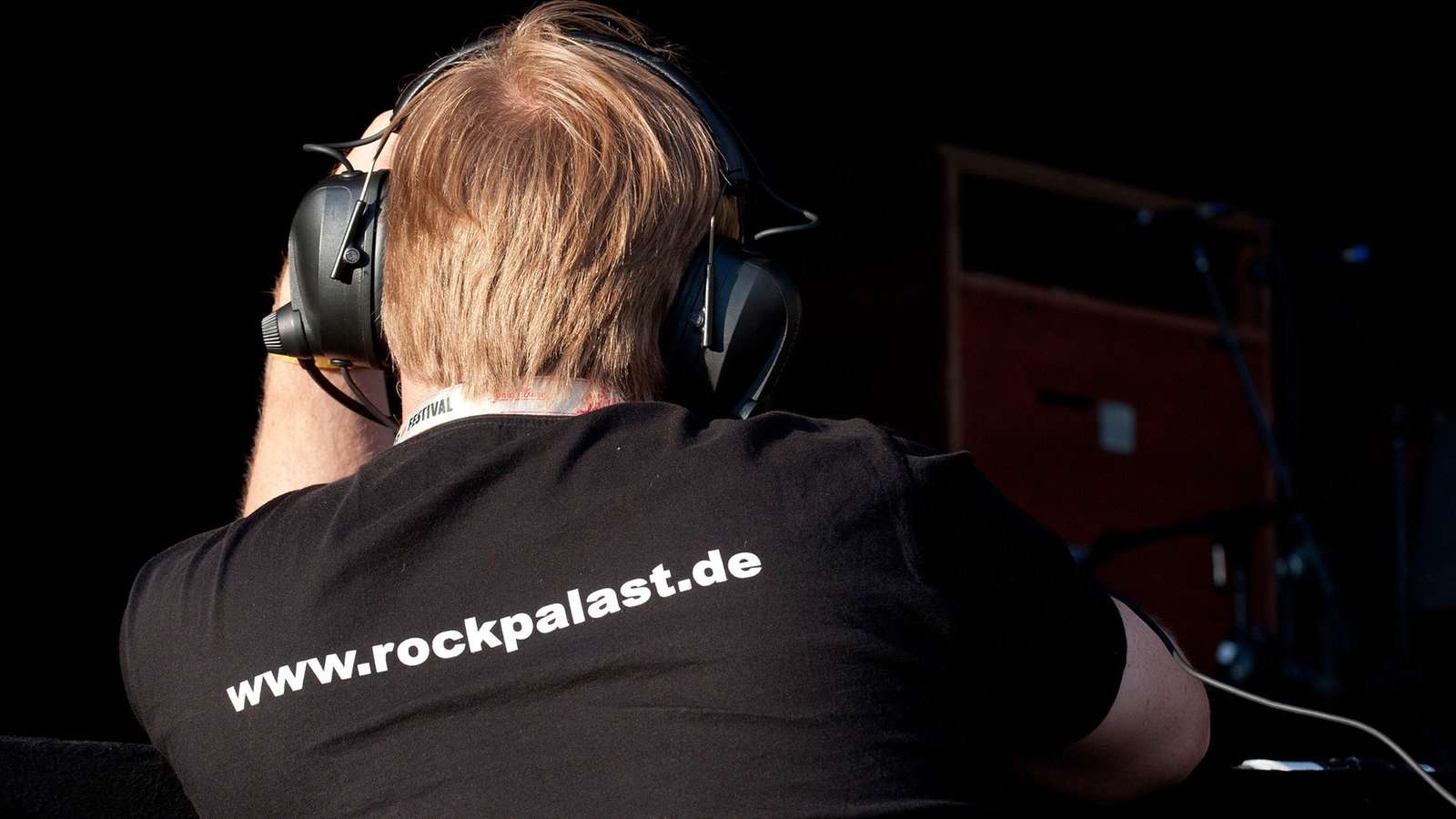 Mann mit Kopfhörern und Rockpalast-Shirt von hinten