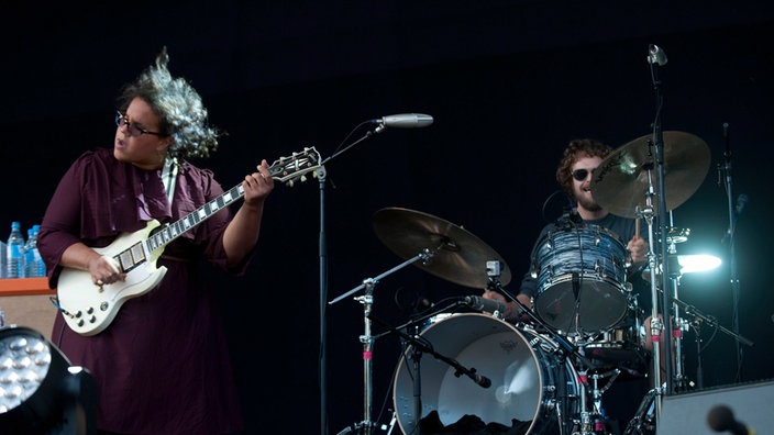Frontfrau der Alabama Shakes hüpft beim Gitarrespielen, im Hintergrund spielt der Schlagzeuger