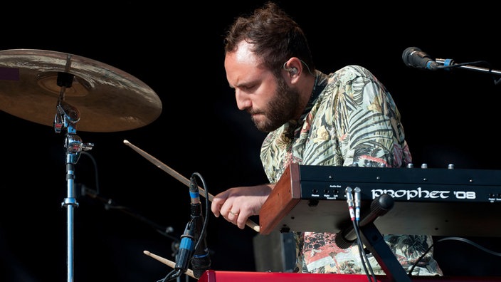Keyboarder der Local Natives spielt auf Schlagzeugteilen, die neben seinen Keyboards aufgebaut sind