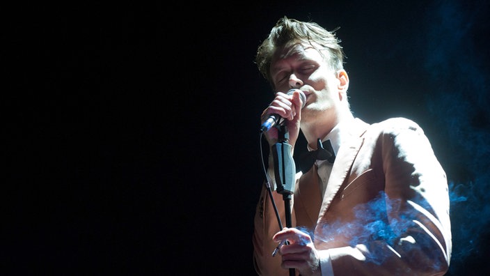 Sänger der Band Efterklang im weißen Anzug mit Fliege singt mit geschlossenen Augen ins Mikrofon