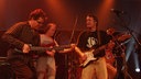 Drei Musiiker der Band "Guru Guru" im roten Bühnenlicht.
