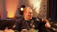 Mitglied der Band "Guru Guru" sitzt auf einem Sofa und erzählt etwas.