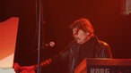 Ein Mann im roten Scheinwerferlicht macht Soundcheck an einem Keyboard.