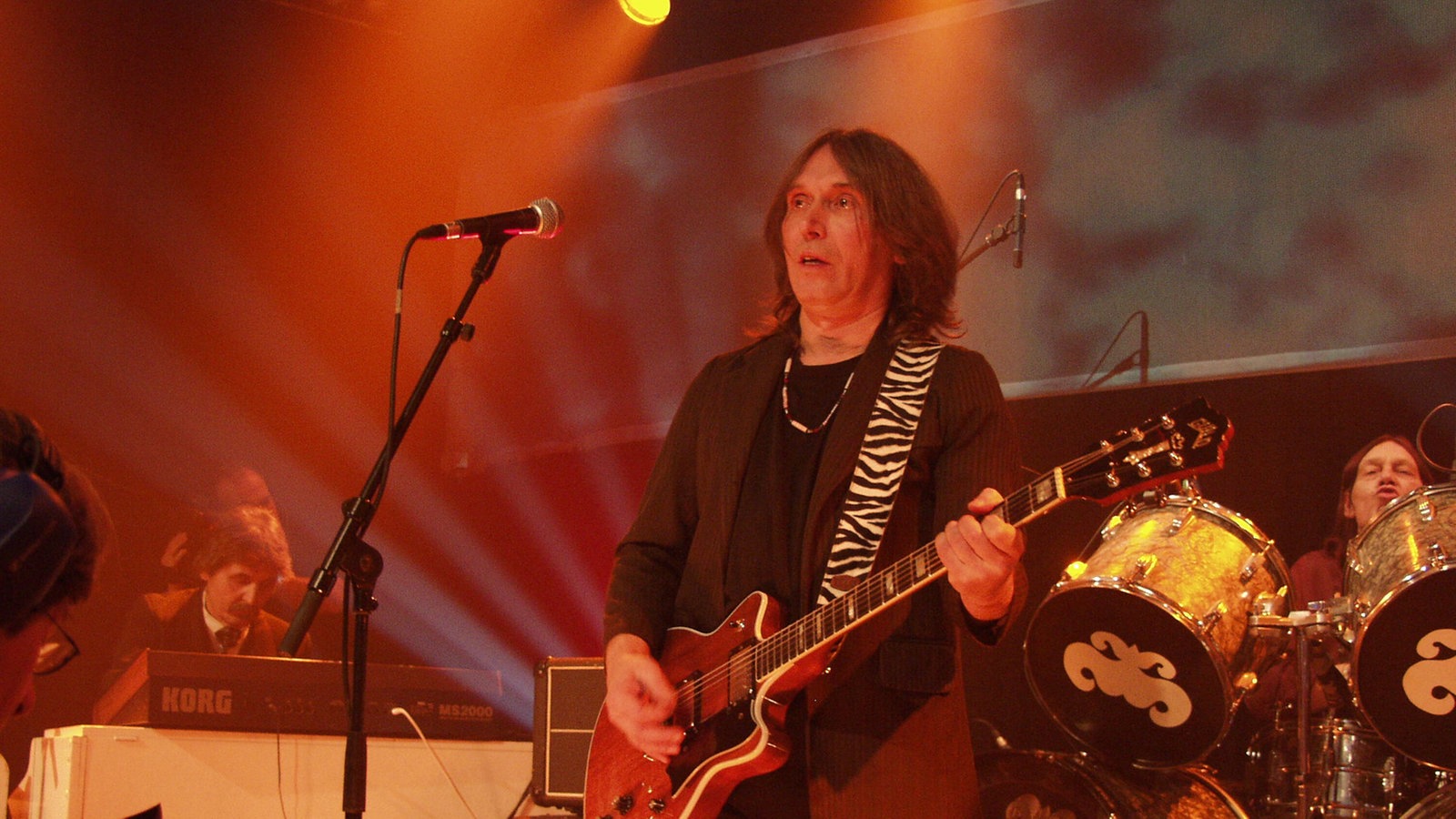 Mann mit langen Haaren und Gitarre auf der Bühne.